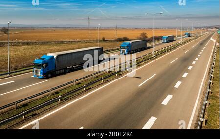 Convoglio di camion Blue trasporto in linea come una carovana o convoglio su una strada di campagna sotto un cielo blu Foto Stock