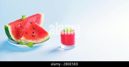 Bevanda estiva, frullato all'anguria in un bicchiere con fette di cocomero fresco su un piatto su sfondo blu pastello, bevanda estiva a base di frutta sana, striscione Foto Stock