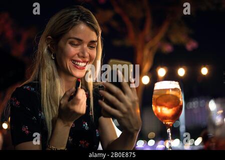 Giovane donna che applica il rossetto al caffè all'aperto Foto Stock