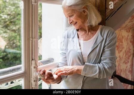 Senior donna in piedi vicino alla finestra Foto Stock