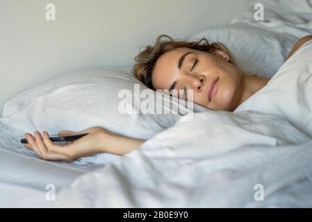 Giovane donna che dorme con lo smartphone Foto Stock