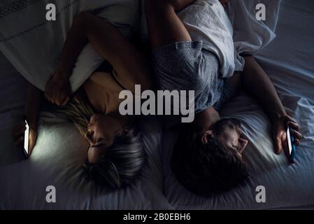 Coppia giovane che usa gli smartphone a letto Foto Stock