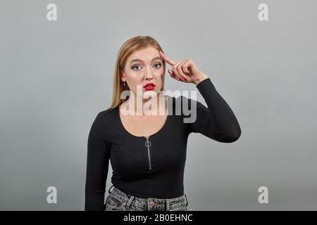 ragazza in giacca su sfondo grigio donna confusa torce indice dito al tempio Foto Stock