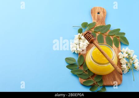 Miele in vaso di vetro e fiori di acacia su sfondo blu, copia spazio Foto Stock