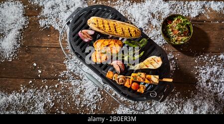 Verdure fresche alla griglia miste servite su un piatto con kebab tofu, mais sul pannocchie, patate dolci e insalata all'aperto su un tavolo invernale con neve in A. Foto Stock