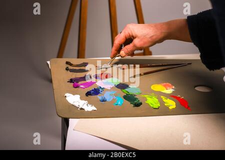 La mano dell'artista lavora con vernici. La mano femminile di un artista anziano lavora con un coltello da tavolozza su una tavolozza. Un primo piano dei colori Foto Stock