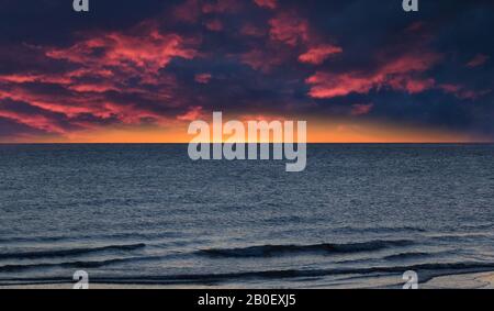 Drammatico rosso scuro e giallo cielo nuvoloso su mare blu con onde Foto Stock
