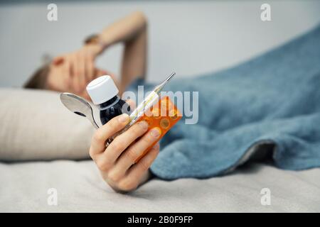 donna malata sdraiata a letto a casa e in possesso di un medicinale in mano Foto Stock