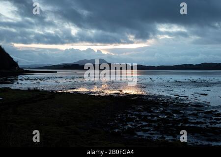 Tramonto su Ardmaddy Bay, Scozia il giorno di Natale, come l'ultimo dei raggi di sole cadere sull'acqua fornendo un riflesso d'oro contro il gloom Foto Stock