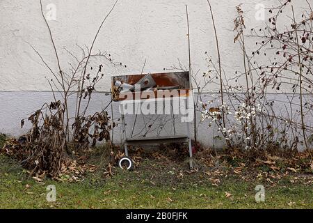 Griglia rotta sulla parete della casa tra la macchia asciutta e l'erba Foto Stock