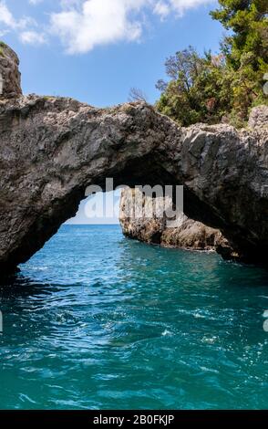 Un arco roccioso scolpito dal mare su acqua blu, lungo le scogliere della Costiera Amalfitana, Italia Foto Stock