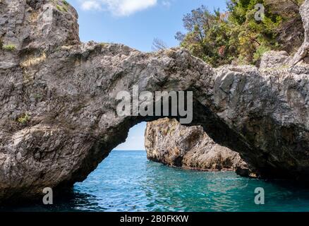 Un arco roccioso scolpito dal mare su acqua blu, lungo le scogliere della Costiera Amalfitana, Italia Foto Stock