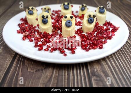 divertenti piccole cifre di orso di banana su piatto bianco dessert sano per i bambini su melograno Foto Stock