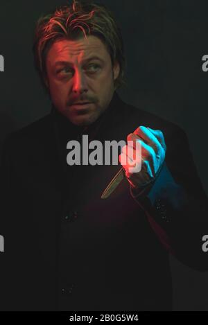 Uomo spaventoso con forbici in mano illuminato da luce rossa e blu. Foto Stock
