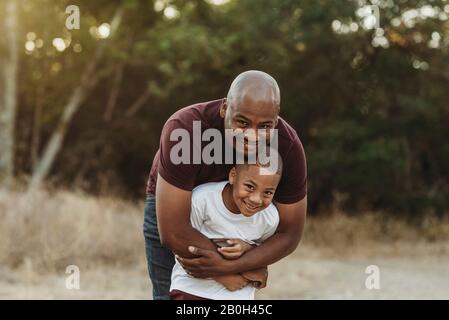 Primo piano di padre e figlio felici abbracciando in campo retroilluminato Foto Stock