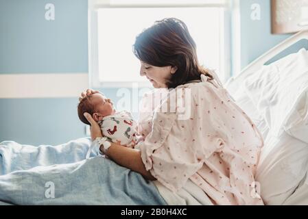 Vista laterale della madre che guarda amorevolmente al figlio neonato in ospedale Foto Stock