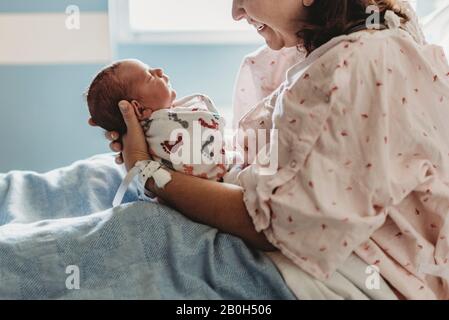 Vista laterale della madre che guarda e sorride al neonato figlio in ospedale Foto Stock