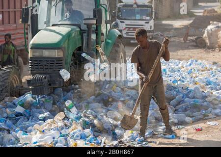 07.11.2019, Adama, Oromiyaa, Etiopia - le bottiglie d'acqua in plastica Vuote vengono premute insieme da un trattore in una strada laterale per essere riutilizzate. Un lavoratore spalma il pla Foto Stock