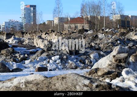 Molta neve velata con un sacco di piccole rocce fotografate durante una soleggiata giornata primaverile a Espoo, Finlandia, febbraio 2019. Edifici sullo sfondo. Foto Stock