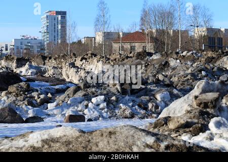 Molta neve velata con un sacco di piccole rocce fotografate durante una soleggiata giornata primaverile a Espoo, Finlandia, febbraio 2019. Edifici sullo sfondo. Foto Stock