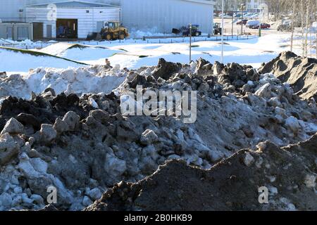 Molta neve velata con un sacco di piccole rocce fotografate durante una soleggiata giornata primaverile a Espoo, Finlandia, febbraio 2019. Edifici sullo sfondo. Foto Stock