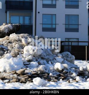 Molta neve velata con un sacco di piccole rocce fotografate durante una soleggiata giornata primaverile a Espoo, Finlandia, febbraio 2019. Edifici sullo sfondo. Foto Stock