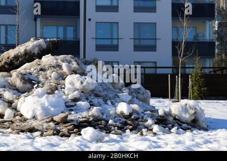 Molta neve velata con un sacco di piccole rocce fotografate durante una soleggiata giornata primaverile a Espoo, Finlandia, febbraio 2019. Edifici sullo sfondo. Foto Stock