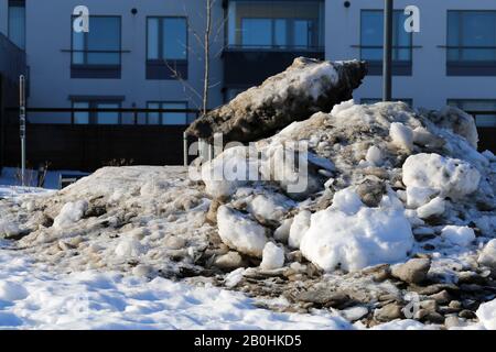 Molta neve velata con un sacco di piccole rocce fotografate durante una soleggiata giornata primaverile a Espoo, Finlandia, febbraio 2019. Edifici sullo sfondo. Foto Stock