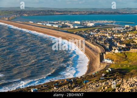 Fortuneswell, Portland, Dorset, Regno Unito. 20th febbraio 2020. Meteo Regno Unito. Vista dalla cima delle scogliere di West Weares attraverso Fortuneswell sull'Isola di Portland a Dorset durante il tardo pomeriggio sole con vento frettoloso e mari accidentati che si infrangono a riva su Chesil Beach a Chiswell. Foto Di Credito: Graham Hunt/Alamy Live News Foto Stock