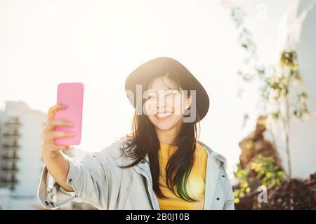 Ragazza asiatica che prende selfie con smartphone mobile all'aperto - Felice donna cinese che si diverte con le nuove tendenze tecnologia app Foto Stock