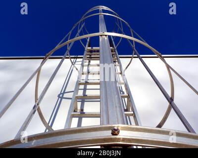 scala di accesso al tetto in alluminio astratta. prospettiva decrescente. gabbia di sicurezza. imbullonata a parete in cemento. luce solare brillante. concetto di industria edile. Foto Stock