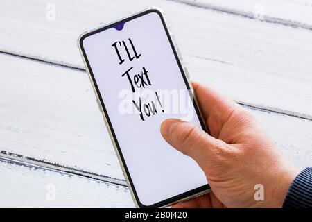 Mano maschile tenendo un telefono con le parole 'ti testo!' sfondo di legno chiaro Foto Stock