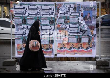 Teheran, Iran. 20th Feb, 2020. Una donna velata iraniana passa davanti a un cartellone elettorale nella strada di Enghelab (Rivoluzione) di Teheran, Iran. Le elezioni parlamentari iraniane del 21 febbraio sono viste come una prova della popolarità del blocco relativamente moderato e pro-riforma del presidente Rouhani. Il suo governo, tuttavia, ha lottato per la maggior parte per mantenere le promesse di campagna per migliorare la vita delle persone mentre l'economia dell'Iran si fa carico delle sanzioni statunitensi. Credito: Rouzbeh Fouladi/Zuma Wire/Alamy Live News Foto Stock