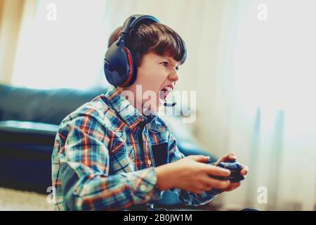 Pazzo dipendente capretto gridando durante il gioco di massa multiplayer video gioco online a casa Foto Stock