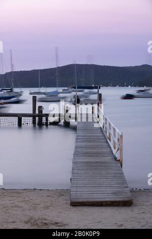 Fisherman on tidal pool jetty su un tramonto viola con yacht che bobbano in acqua Foto Stock