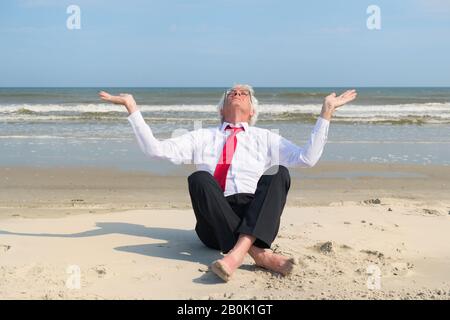 Uomo d'affari senior seduto in meditazione in spiaggia Foto Stock