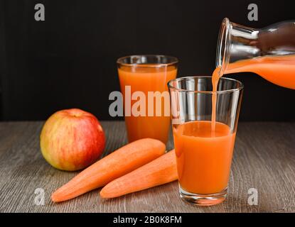 Il succo di mela della carota viene versato dalla bottiglia in un bicchiere. Ci sono carote e mele sul tavolo. Foto Stock