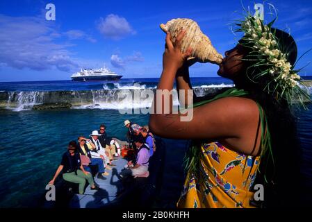 ISOLE COOK, ISOLA DI ATIU, RAGAZZA CHE SOFFIA IN SEASHELL (CORNO), SALUTARE I TURISTI A ZODIAC Foto Stock