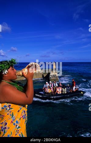 ISOLE COOK, ISOLA DI ATIU, RAGAZZA CHE SOFFIA IN SEASHELL (CORNO), SALUTARE I TURISTI A ZODIAC Foto Stock