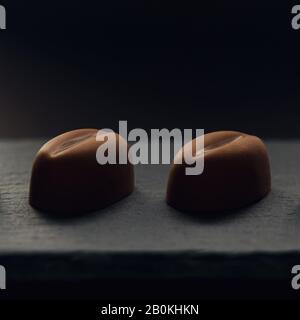 Due pezzi di caffè a forma di fagiolo cioccolato su vassoio di pietra nera Foto Stock