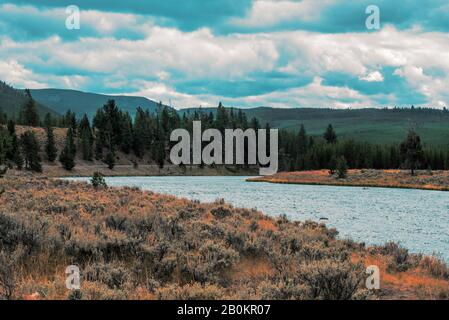 Ambiente tranquillo, fiume che attraversa la valle con campi e foreste sotto il cielo blu con le nuvole. Foto Stock