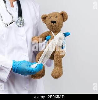 la medic femminile contiene orsacchiotto marrone e bendaggi zampa con bendaggio di garza bianca, concetto di pediatria e trattamento animale Foto Stock