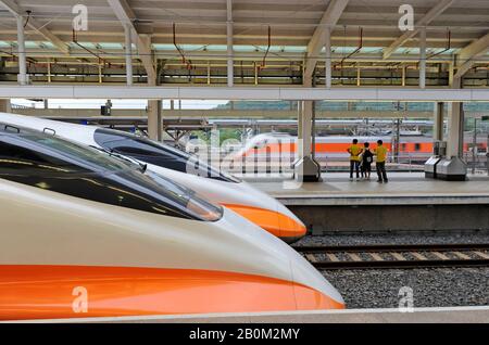 I passeggeri guardano un treno convenzionale che passa dalla stazione di Zuoying a Kaohsiung, mentre due treni superveloci HSR attendono di partire per Taipei, Taiwan Foto Stock