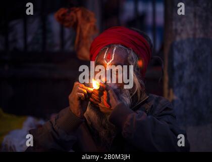 Un Sadhu (l'uomo santo indù) fuma marijuana usando un chillum un tradizionale tubo di argilla come offerta Santa alla vigilia di Maha Shivaratri.Maha Shivaratri, 'la Grande Notte di Shiva', una festa indù è celebrata in onore di Lord Shiva, che è osservato da canti preghiere e digiuno. Foto Stock