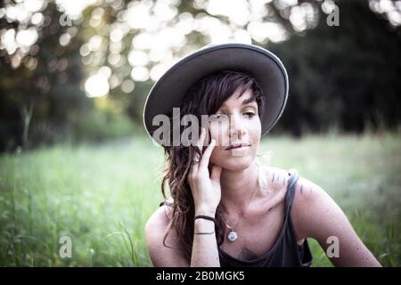 la ragazza naturale con i freckles e i tatuaggi siede pacificamente in erba lunga Foto Stock