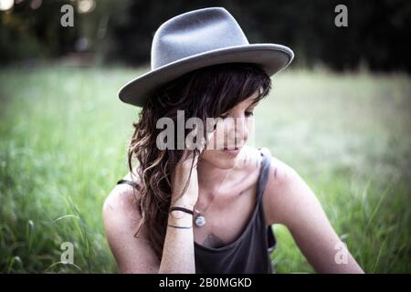 la ragazza naturale con i freckles e i tatuaggi siede pacificamente in erba lunga Foto Stock