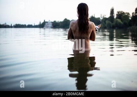 vista posteriore di una donna forte che tiene un piccolo cane nel lago naturale di berlino Foto Stock