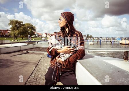 forte donna asiatica si trova al molo d'acqua con due cani piccoli al sole Foto Stock