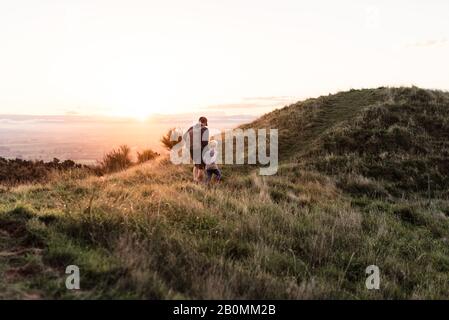 Padre e figlio camminano sulla collina al tramonto Foto Stock