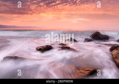 Un'esposizione lunga di un tramonto dell'oceano che Cattura il flusso molle Dell'Acqua di mare Che Corre a Shore Foto Stock